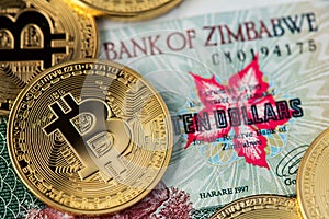 Golden Bitcoin coins new virtual money on Zimbabwe hyperinflation banknote close up image.