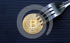Golden bitcoin with fork on wood.
