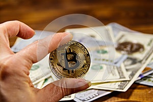 Golden bitcoin in hand against one hundred dollar bills