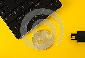 Golden bitcoin, keyboard and flash drive on a yellow background top view