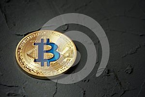 Golden bitcoin lying on a dark, plastered surface