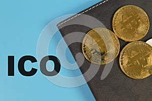 Golden bitcoins and notebook on blue background with text ICO stands for Initial Coin Offering