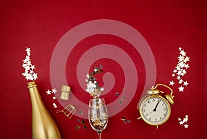 Golden bottle of champagne, glass, alarm clock and confettie over the red background. Party, new year, christmas celebration