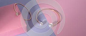 Golden bracelets with gemstones on pink and purple background with copy space