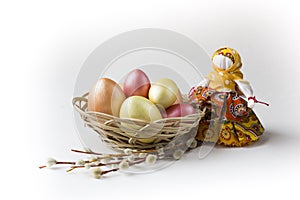 Golden, bronze and pink Easter eggs in basket with pussy willow and textile doll on white.