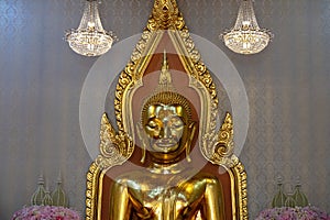 Golden buddha statue, portrait shot. Crystal chandeliers on either side.