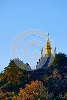 Golden buddhist stupa of Wat Chom Si at the summit of Mt. Phou Si, in Luang Prabang, Laos. Low angle view from the city.