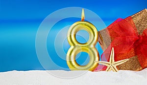 Golden candle number 8 with gift with red bow and starfish on beach. 8th of March, International Women\'s Day, birthday