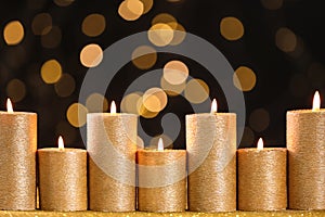 Golden candles burning on table against defocused lights