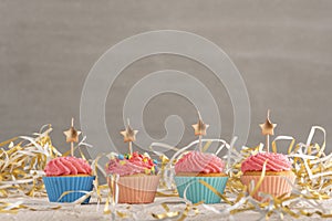Golden candles in the shape of star on cupcakes. Muffins with pink buttercream frosting on festive tinsel background. Copy spacve