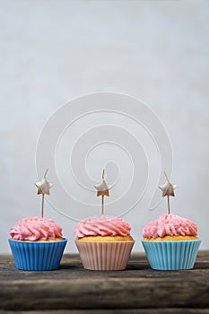Golden candles in the shape of star on cupcakes with pink buttercream frosting. Birthday cupcakes on wooden table. Gray background
