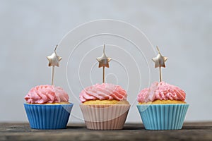 Golden candles in the shape of star on cupcakes with pink buttercream frosting. Birthday cupcakes on wooden table. Gray background