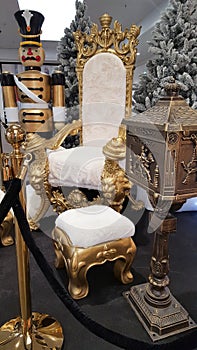 Golden chair with white velvet cushions next to a festively decorated Christmas tree and gifts decoration at Christmas market for