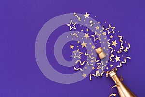 Golden champagne bottle with confetti stars and party decorations on violet background. Christmas, birthday or New Year card