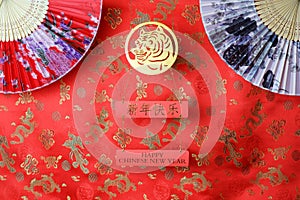 Golden chinese tiger symbol and pair of chinese bamboo paper fans on red fabric with traditional chinese ornament of birds and