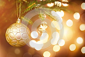 Golden Christmas ball on a live branch of a fir tree with Golden lights of garlands in defocus. New year, Christmas, holiday
