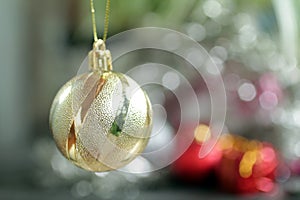 Golden Christmas ball ornament hanging on a blur tree bokeh light festive background. Closeup of single gold Christmas ball