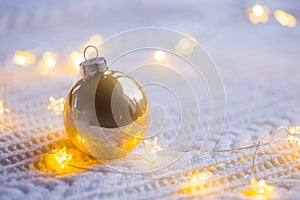 Golden Christmas ball with warm garland lights on white knitted