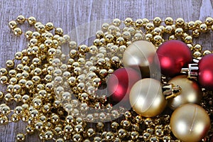 a Golden Christmas chain lies on the wooden table and on top of it there are traditional red and gold Christmas balls