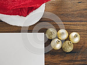 Golden Christmas and New years eve balls on a red Santa Claus hat on white surface, Blank white paper in the left bottom corner