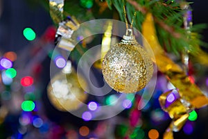 Golden Christmas tree balls on a branch, in the background are the lights of garlands and serpentine