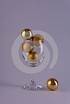 golden christmas tree balls in a wine glass on a gray background