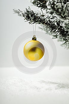 Golden Christmas tree toy ball on artificial fir tree with snow on white background. A minimalistic new year.