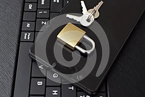 Golden color locked padlock keys and black smartphone on keyboard