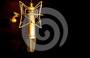 Golden color microphone detail in music and sound recording studio, black background, closeup