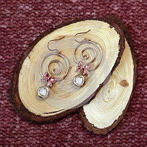 Golden colored handmade earrings on wooden slabs on brown textured fabric background