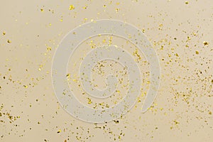 Golden confetti on beige paper trendy background. Festive holiday backdrop. Birthday congratulations Christmas New Year.