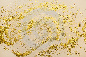 Golden confetti on beige paper trendy background. Festive holiday backdrop. Birthday congratulations Christmas New Year.