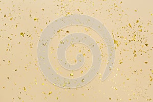 Golden confetti on beige paper trendy background. Festive holiday backdrop. Birthday congratulations Christmas New Year.