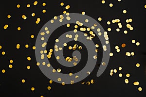 Golden confetti on black background. Festive holiday backdrop. Birthday congratulations Christmas New Year.