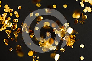 Golden confetti on black background. Festive holiday backdrop. Birthday congratulations Christmas New Year.