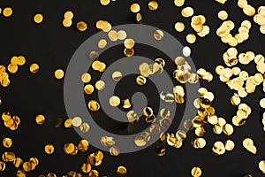 Golden confetti on black background. Festive holiday backdrop. Birthday congratulations Christmas New Year.