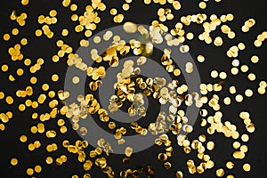Golden confetti on black background. Festive holiday backdrop. Birthday congratulations Christmas New Year.