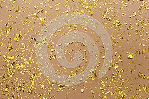 Golden confetti on earthy brown paper trendy background. Festive holiday backdrop. Birthday congratulations Christmas New Year.