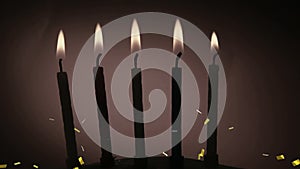 Golden confetti falling over silhouette of multiple burning candles against grey background