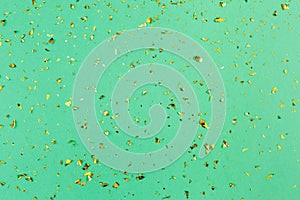 Golden confetti on trendy green paper background. Festive holiday backdrop. Birthday congratulations Christmas New Year.