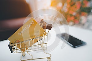 Golden credit card in the Shopping Cart against smartphone on white table