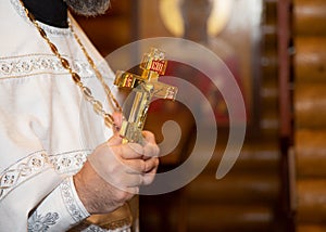 A golden cross in the hands of a priest. A male priest holds a large Orthodox cross