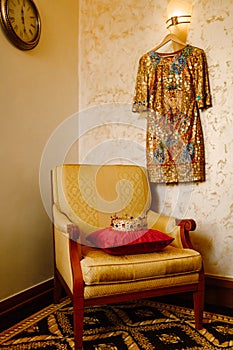 A golden crown encrusted with red and blue gemstones, on a red pillow on a chair in the interior of the room. A gold