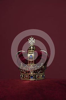 Golden crown on a velvet cushion on a deep red background with copy space in a vertical image