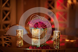 Golden cube vase with red roses arrangement on the table with reflection