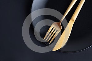 Golden cutlery on plate on dark
