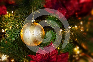 Golden decorative ball hanging on a branch of a Christmas tree in the light of garland. Phot backdrop decoration for Christmas