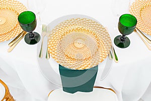 Golden dishes, green wine glasses and napkins. Catering concept. Interior of tent for wedding dinner, ready for guests