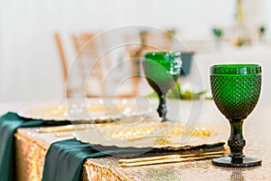 Golden dishes, green wine glasses and napkins. Catering concept. Interior of tent for wedding dinner, ready for guests