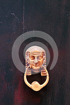 Golden door knocker with an Egyptian face on a wooden door, golden in color, carved